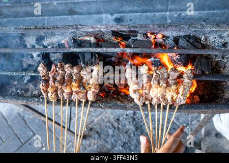 Koch grillt indonesisches Sate Klatak-Ziegenfleisch auf Metallspießen über flammendem Holzkohle, authentisches Straßenfood aus Yogyakarta. Stockfoto