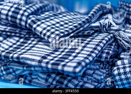 Nahaufnahme eines gestapelten Haufens traditioneller blau-weiß karierter Baumwoll-Keffiyeh-Schals mit Fransendetails auf einem Markt in Kairouan, Tunesien Stockfoto