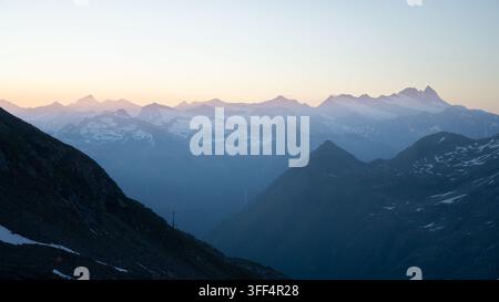 Panoramischer Alpen-Sonnenaufgang vom Grossvenediger mit geschichteten Bergkämmen und schneebedeckten Gipfeln, die im sanften Morgendlicht leuchten, Österreichische Alpen Stockfoto