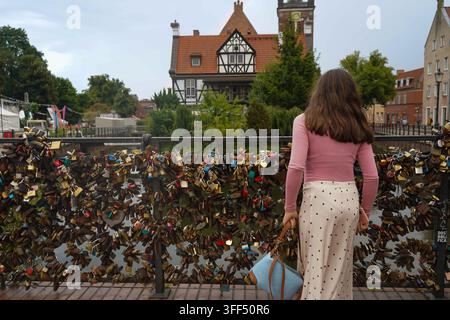 Ein Teenager blickt vom einer mit Liebesschlössern bedeckten Brücke in Danzig, Polen, über den Radunia-Kanal zum historischen Dwór Młynarzy-Gebäude. Stockfoto