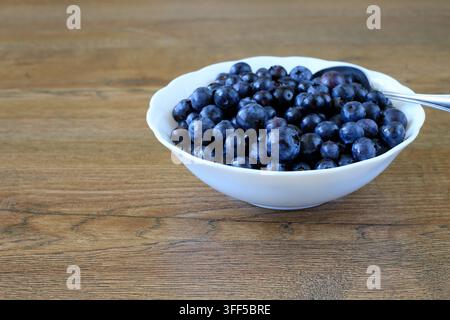 Bio-Heidelbeeren in einer weißen Schüssel auf einer Holzarbeitsplatte. Gesunder Lebensstil, Obstsnacks, ausgewogene Ernährung und Antioxidans-Therapie. Stockfoto
