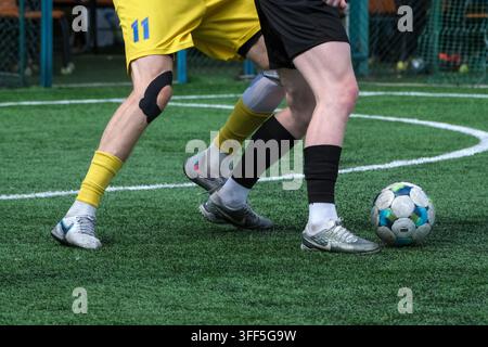 Kiew, Ukraine – 05. September 2026: Futsal-Spieler in schwarzen und gelben Trikots im engen Körperkontakt, die während eines Mini-Fußballspiels um den Ball kämpfen Stockfoto