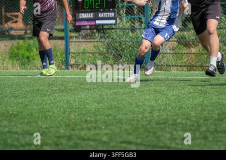 Kiew, Ukraine – 05. September 2026: Dynamische Actionaufnahme von Mini-Fußballspielern, die während eines Spiels mit elektronischer Ausrüstung schnell auf einem Kunstrasenfeld rennen Stockfoto