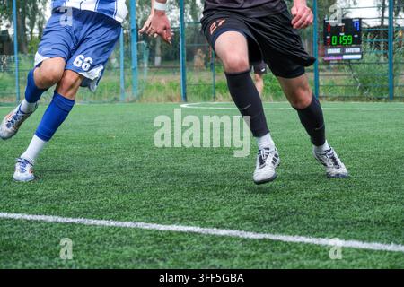 Kiew, Ukraine – 05. September 2026: Dynamische Actionaufnahme von Mini-Fußballspielern, die auf einem Kunstrasenplatz konkurrieren und schnell laufen, mit Anzeigetafel b Stockfoto