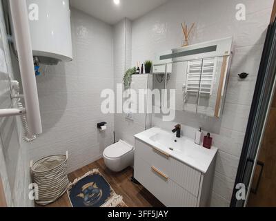 Modernes Wohnbadezimmer-Interieur mit weißen strukturierten Keramikwandfliesen und braunen holzeffektiven Bodenfliesen. Der Raum umfasst eine Wandmontage Stockfoto