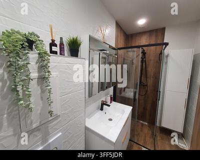 Modernes Badezimmerinterieur mit weißen strukturierten Wandfliesen und zeitgenössischen Armaturen. Der Raum umfasst einen weißen Waschtischschrank mit integriertem Stockfoto