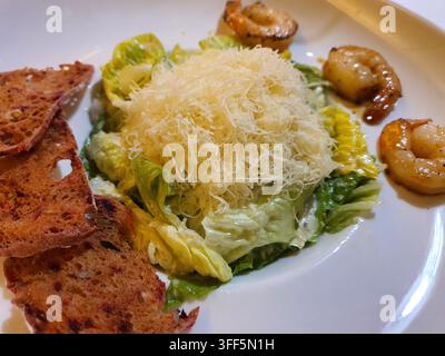 Eine Nahaufnahme eines Gourmet-Caesar-Salats, der auf einem weißen Teller serviert wird. Das Gericht zeigt frische Römersalatblätter, die mit cremigem Caesar-Dressing überzogen sind, Stockfoto