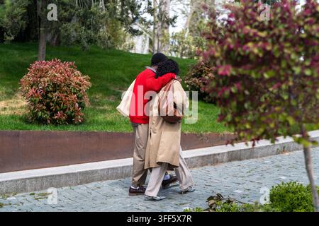 Stylisches schwarzes Paar geht Arm in Arm durch den gepflegten grünen Stadtpark zusammen bei einem Date Stockfoto