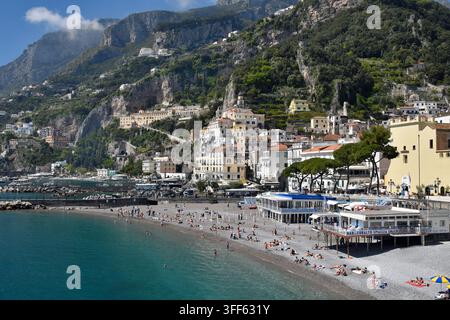 Eine Aussicht über den Strand in Amalfi an einem sonnigen Apriltag mit Bars, Restaurants und Hotels mit steilen Klippen, Küstenstraßen und Tunneln im Hintergrund. Stockfoto