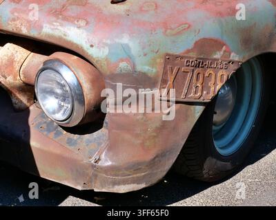 Nahaufnahme eines runden Chrom-Scheinwerfers und eines stark verrosteten Kotflügels an einem klassischen Oldtimer-Pickup. Ein gealtertes Vintage-Kennzeichen und Blau Stockfoto
