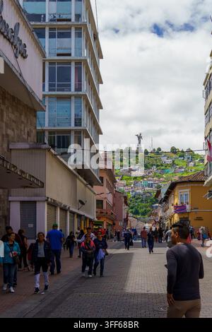 Fußgänger schlendern eine belebte Straße in Quito, Ecuador, entlang, mit der El-Panecillo-Statue auf dem Hügel Stockfoto
