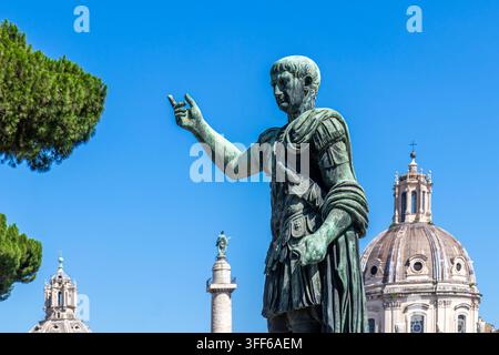 Bronzestatue des Kaisers Trajan mit der Trajanssäule und der Kirche des Allerheiligsten Namens Marias im Hintergrund, Rom Stockfoto