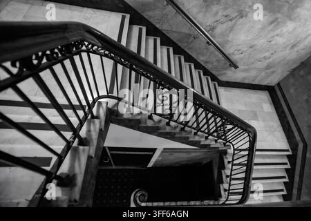 Schwarz-Weiß-Hochwinkelaufnahme einer historischen Marmortreppe mit schmiedeeisernem Geländer. Stockfoto
