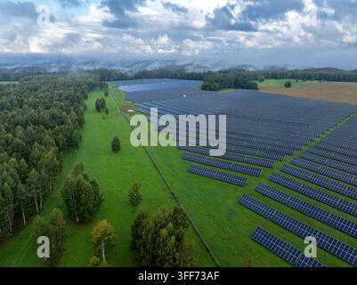 Luftbild einer großen Solaranlage neben Wald und ländlicher Landschaft unter dramatischem bewölktem Himmel Stockfoto