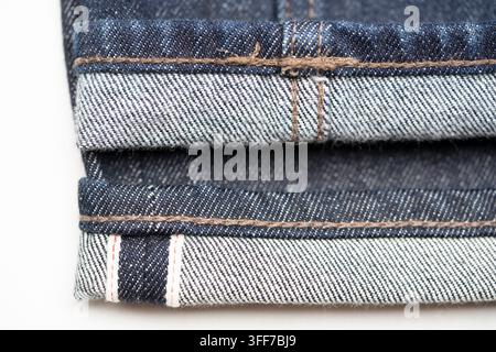 Selvedge-Denimjeans von Uniqlo mit roter Ohrnähte auf weißem gewebtem Selbstrand (unten) reguläre Uniqlo-Denimjeans (oben) Stockfoto