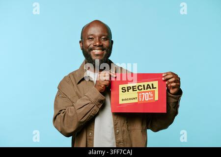 Porträt eines lächelnden afroamerikanischen Mannes mittleren Alters, der eine Rabattkarte während des Black Friday-Einkaufs hält. Konzept, das Verkaufsförderung repräsentiert Stockfoto