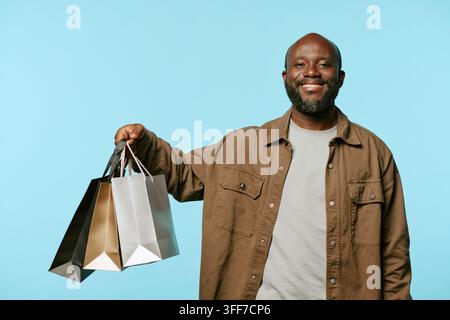 Porträt eines lächelnden afrikanisch-amerikanischen Mannes mittleren Alters, der Einkaufstüten während eines Black-Friday-Sales hält. Bild geeignet für Einzelhandels-Marketingkampagnen und Stockfoto