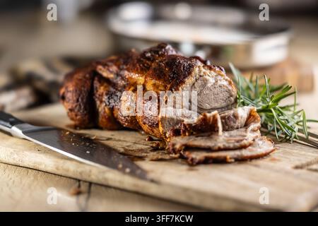 Leckeres gebratenes Schweinehals mit knuspriger Kruste ist mit frischem Rosmarin garniert und auf einem Holzbrett filetiert. Dieser professionelle kulinarische Shot wird pass Stockfoto