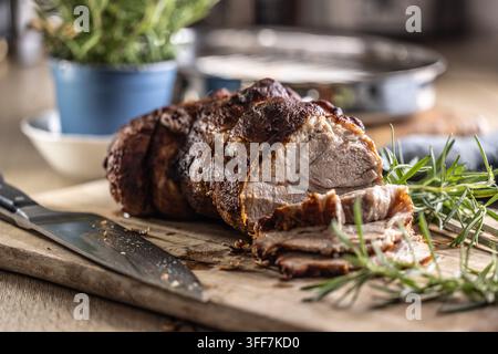 Leckeres gebratenes Schweinehals mit knuspriger Kruste ist mit frischem Rosmarin garniert und auf einem Holzbrett filetiert. Dieser professionelle kulinarische Shot wird pass Stockfoto