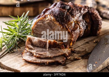 Leckeres gebratenes Schweinehals mit knuspriger Kruste ist mit frischem Rosmarin garniert und auf einem Holzbrett filetiert. Dieser professionelle kulinarische Shot wird pass Stockfoto