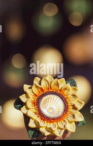 Ein solarbetriebener sonnenblumenförmiger Scheinwerfer vor einem unscharfen Hintergrund mit Bokeh-Lichtern Stockfoto
