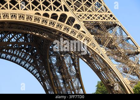 Nahaufnahme des kunstvollen Metallgitterwerks und des architektonischen Bogens des Eiffelturms unter einem klaren blauen Himmel in Paris, Frankreich Stockfoto