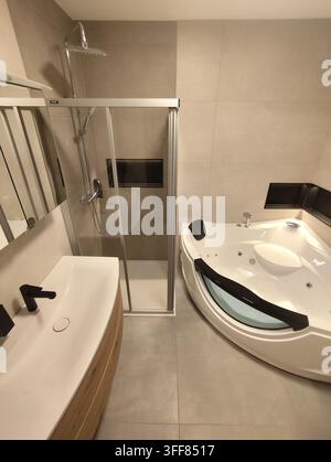 Badezimmerinnenraum mit Waschtisch-Glascabinett und Whirlpoolwanne im minimalistischen Stil. Stockfoto