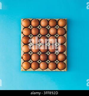 Braune Eier in Kartonschachtel auf blauem Hintergrund. Minimales Lebensmittelkonzept. Flachlage, Blick von oben. Stockfoto