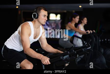 Entschlossener junger Mann trainiert mit Spin-Bike in der Fitnesshalle während eines Ganzkörper-Workouts Stockfoto