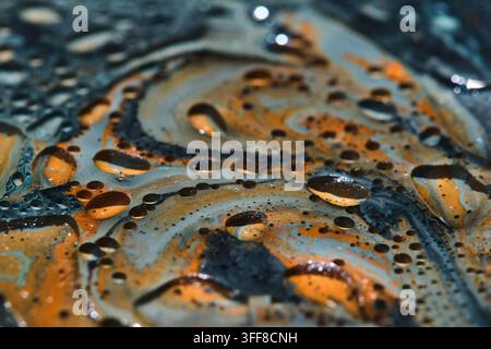 Nahaufnahme abstrakter flüssiger Hintergrund mit glänzenden Öltropfen über orangefarbenen und blauen Farbfäden Stockfoto
