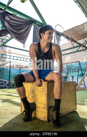 Junger Athlet lächelt, während er in einem Fitnessstudio im Freien ruht Stockfoto