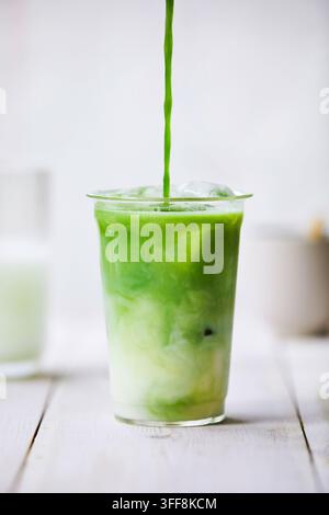 Matcha Latte in einem Glas. Matcha und Milch vermischen sich, während der Matcha von oben in das Glas gegossen wird. Helle, frische und freundliche Atmosphäre. Stockfoto