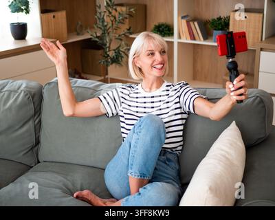 Zufriedene Schöpferin nimmt ein Gesprächsvideo für ihre Follower auf, während sie bequem auf der Couch sitzt. Stockfoto