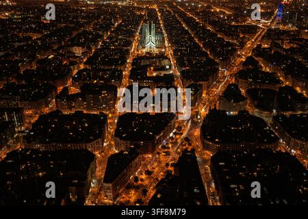 Luftbild der Sagrada Familia bei Nacht beleuchtet, zeigt das rasterartige Stadtlayout und die leuchtenden Straßenlaternen des Eixample-Bezirks in Barce Stockfoto