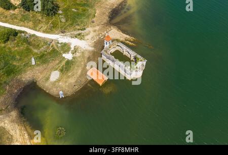 Luftbild der versunkenen Kirche St. Nikolaus, teilweise im Mavrovo-See versunken, mit grasbewachsenen Ufern und einer kleinen Struktur in Mavrovo, Gemeinde Stockfoto