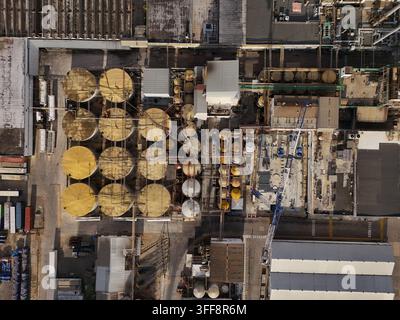 Luftbild einer Industrieanlage mit Reihen großer kreisförmiger Lagertanks, komplexer Rohrleitungstechnik und Baugeräten in Santo Domi Stockfoto