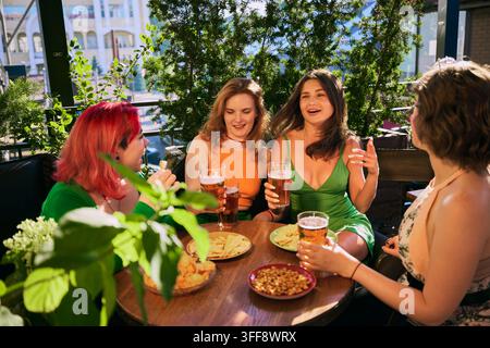 Glückliche Frauen lachen mit Biergläsern und Snacks an einem sonnigen Außentisch Stockfoto