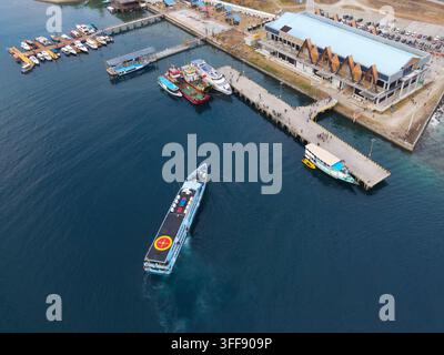 Luftaufnahme des Waisai-Hafens mit einem Fährboot, das am Pier anlegt, umgeben von festgemachten Booten, klarem Wasser und dem Terminalgebäude in Raja Ampat Stockfoto