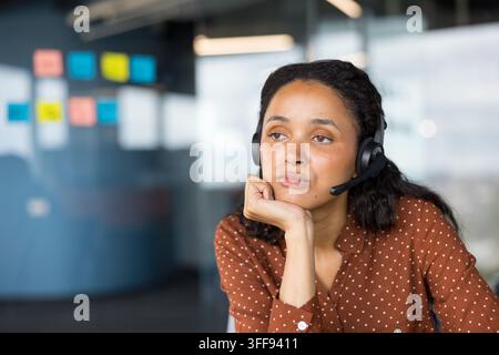 Frau mit Headset, die nachdenklich und gelangweilt aussieht, während sie ihr Kinn auf die Hand stützt und in einem Büroarbeitsumfeld in einem Callcenter oder Kundenservice arbeitet Stockfoto