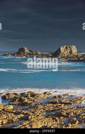 061 Das warme Licht der Morgendämmerung erhellt die Meeresfelsen von La Forcana am Strand von Playa Gueirúa, der Himmel ist von einer dicken dunklen Wolke bedeckt. Cudillero-Asturien-Spanien. Stockfoto