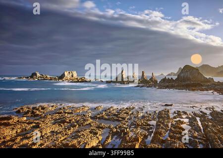 062 Lebendiger Morgen über Playa Gueirúa Beach und seiner Reihe scharfer Kliffen, die von einer dicken dunklen Wolke mit der Sonne darüber begleitet werden. Cudillero-Asturien-Spanien. Stockfoto