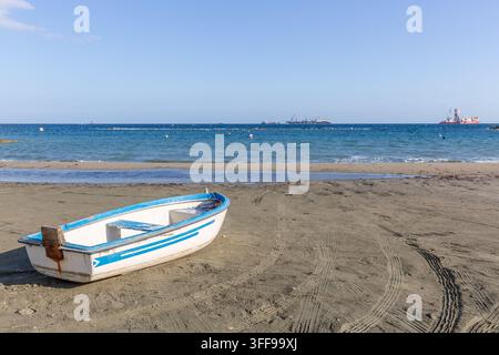 Ein kleines weißes und blaues Boot, das auf dem Sand des Strandes von Limassol ruht, mit einem ruhigen Meer und einem blauen Himmel im Hintergrund. Stockfoto