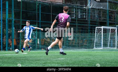 Fußballspieler in blau-weißer Uniform schießt, während ein Gegner während eines Fußballspiels im Freien auf einem Kunstrasenfeld in Kiew verteidigt, U Stockfoto
