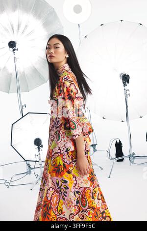 Redaktionelles Studio-Fashion-Bild eines jungen asiatischen FEMALE-Modells in einem warmtonigen orange-braunen Paisley-Print-Maxikleid, in einer anderen Pose aufgenommen. Stockfoto