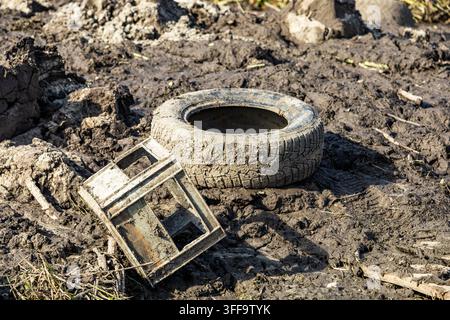Ein weggeworfener Autoreifen und eine Plastikbox, die im dicken Schlamm liegen, zeigen Probleme mit unsachgemäßer Müllentsorgung und Umweltverschmutzung. Stockfoto