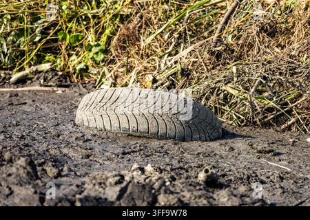 Nahaufnahme eines alten Gummireifens, der halb im schwarzen Schlamm vergraben ist und Umweltverschmutzung und illegale Entsorgung veranschaulicht. Stockfoto