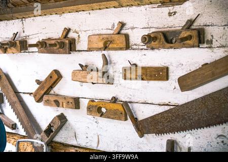 Sammlung klassischer Holzschneidewerkzeuge, die auf rauen Brettern in einem rustikalen Schuppen mit Spuren alter Sägen und Bänke angeordnet sind, die handwerkliches Können und das Zeitlose feiern Stockfoto