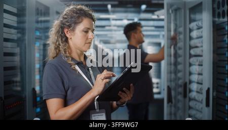 In einem modernen Rechenzentrum verwendet eine Ingenieurin ein digitales Tablet, während ein Kollege die Serverregale überprüft. Mobile Cloud-Diagnostik und Teamzusammenarbeit gewährleisten die Stabilität des High-Tech-Netzwerks. Konzept der Teamarbeit. Stockfoto