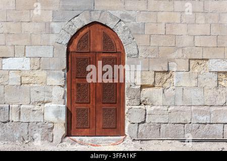 Moderne Holztür in einem spitz zulaufenden Steinbogen der mittelalterlichen Fatimiden-Stadtmauer in Bab al-Futuh, Islamisches Kairo, Ägypten Stockfoto