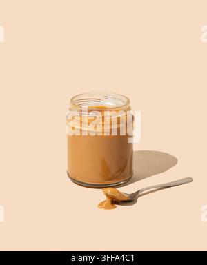 Erdnussbutter oder Karamellsoße im Gläser auf isoliertem beigem Hintergrund mit Löffel und Schatten. Konzept für einen leckeren und gesunden Snack zum Frühstück. Frei Stockfoto